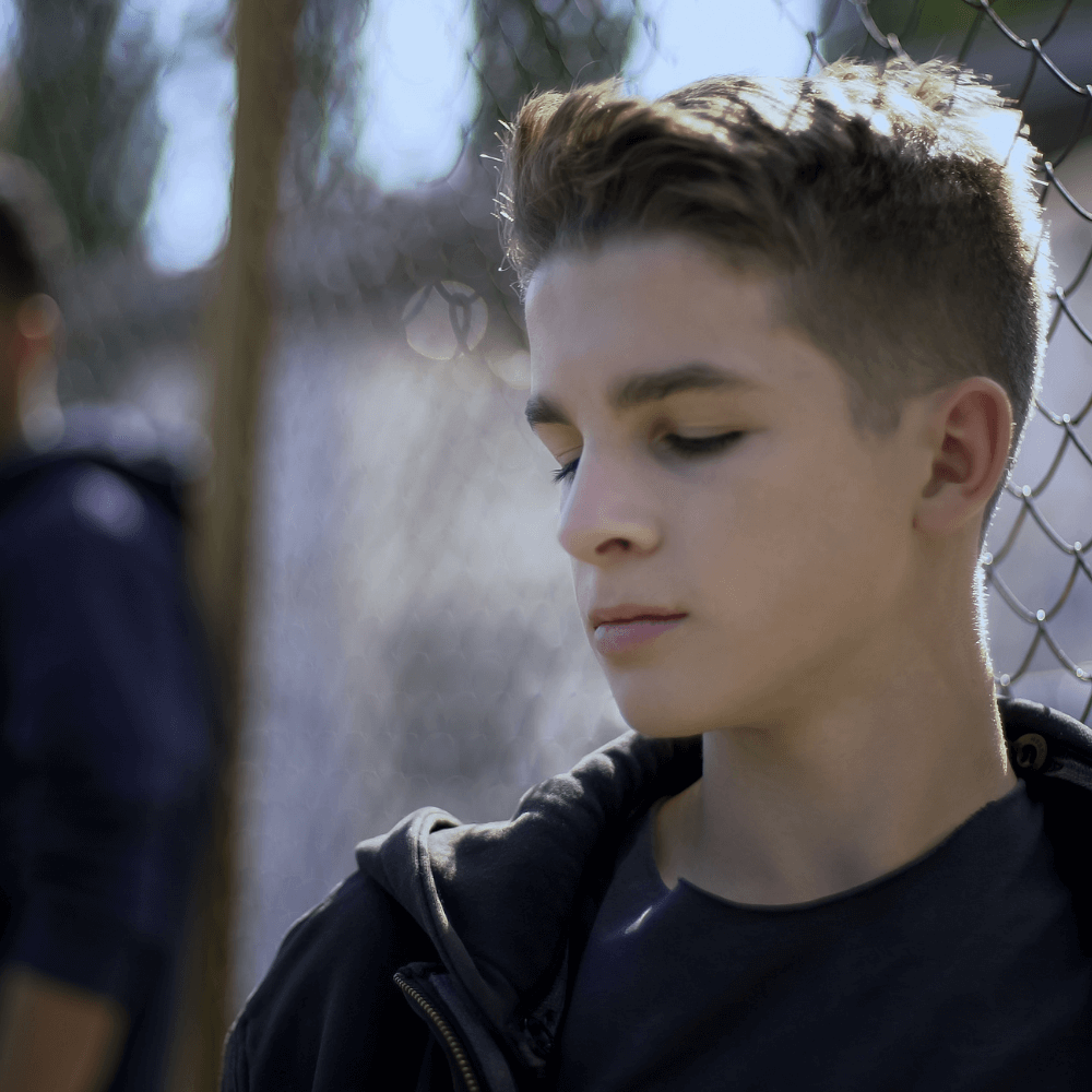 Jeune adolescent adossé à un grillage
