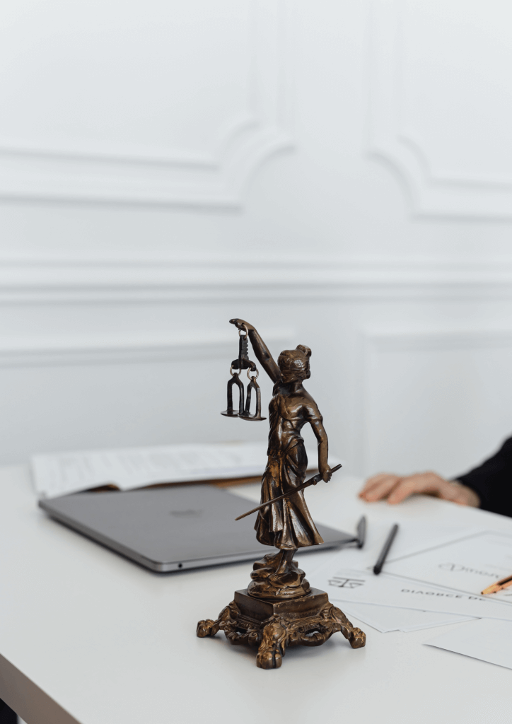 Photo d'une statuette de Thémis, déesse de la justice, en bronze, posée sur un bureau avec un ordinateur portable et quelques feuilles